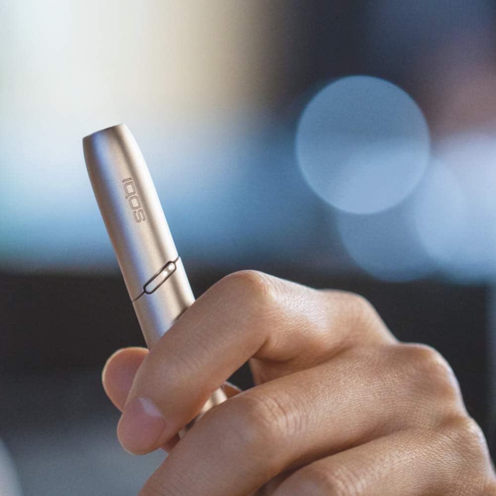 Hand holding a silver iqos 3 device with a blurred background